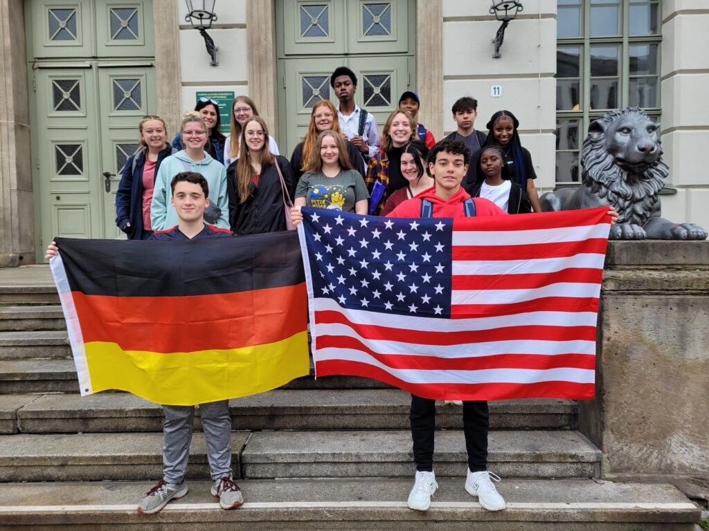 A group of 15 American high school students and their adviser in Germany holding US and German flags.