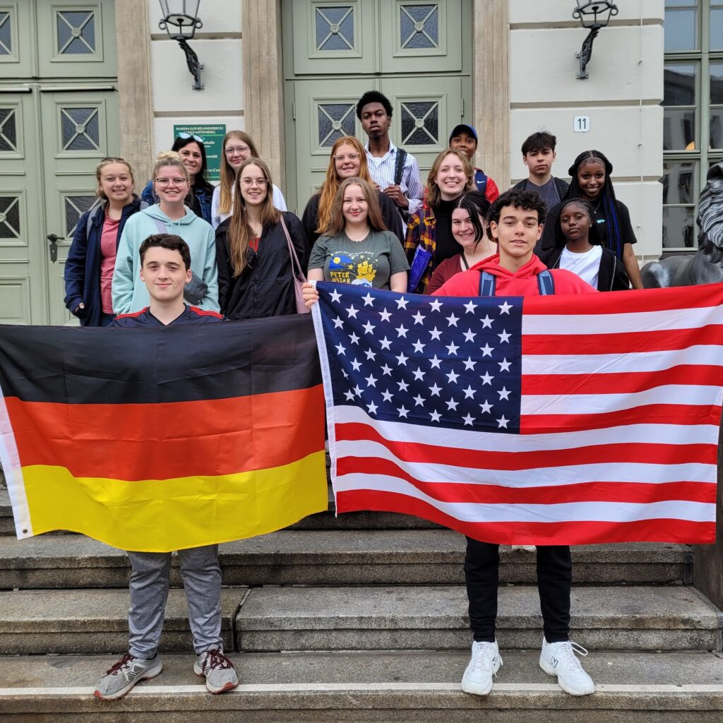 A group of 15 American high school students and their adviser in Germany holding US and German flags.