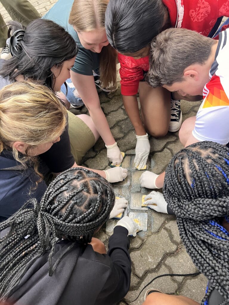 Students cleaning Stolpersteines, or “stumbling blocks,” commemorative brass plaques memorializing Holocaust victims and their families.