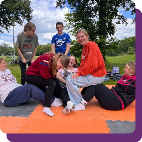 A group of teens work together to build a human pyramid. Smiles and laughter are all around.