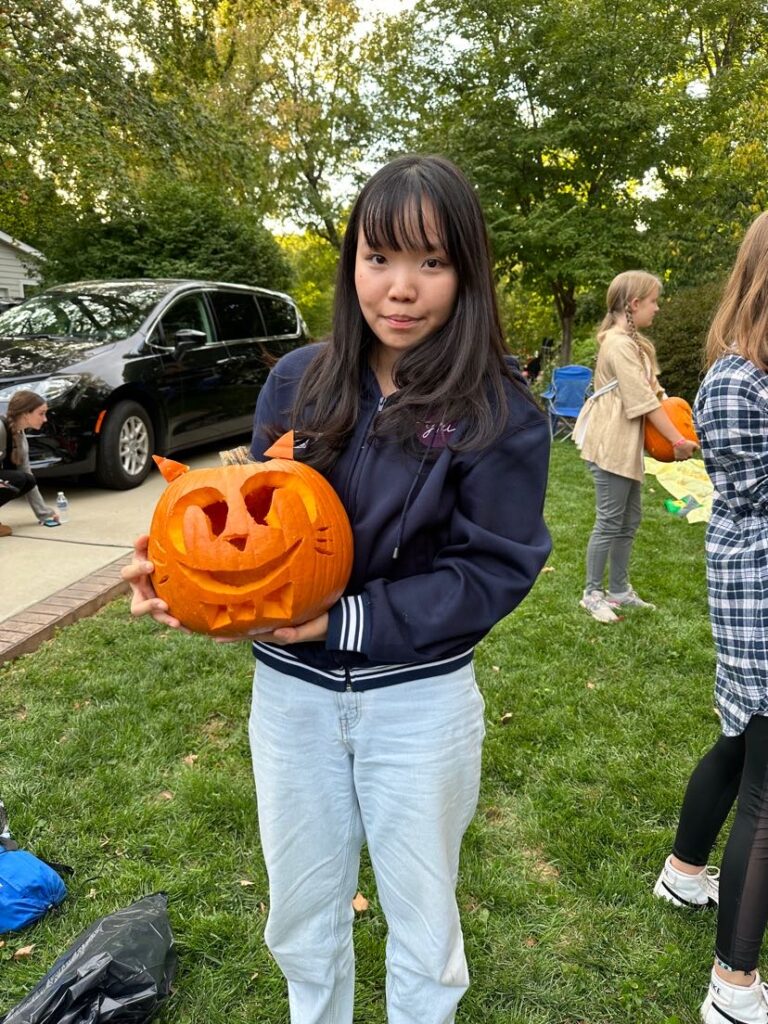 An exchange student holding a freshly carved pumpkin made to look like a cat.