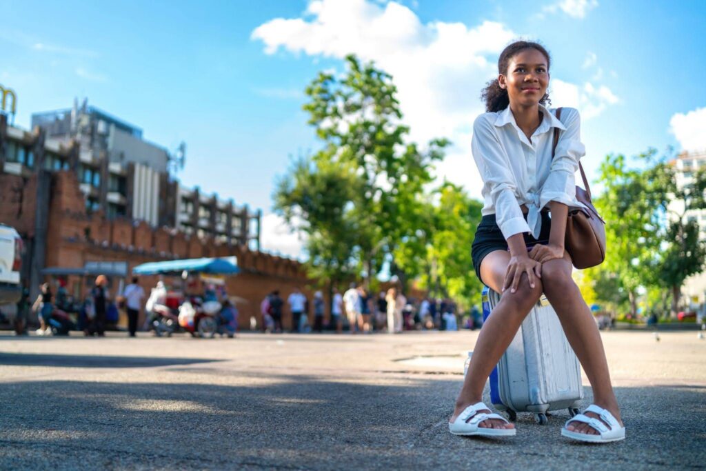 Anxious teen exchange student experiencing culture shock sitting on luggage alone outdoors while adjusting to life abroad